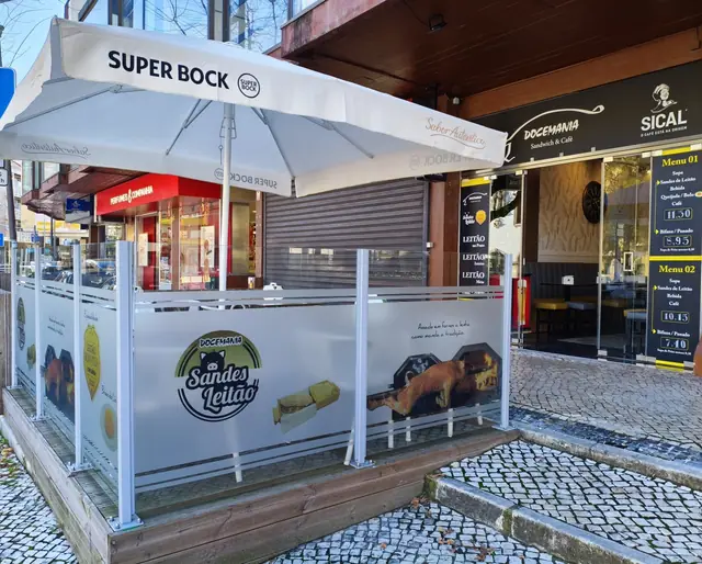 Esplanada com guarda-sol e para-ventos decorados com o selo Sandes Leitão e imagens de leitão assado