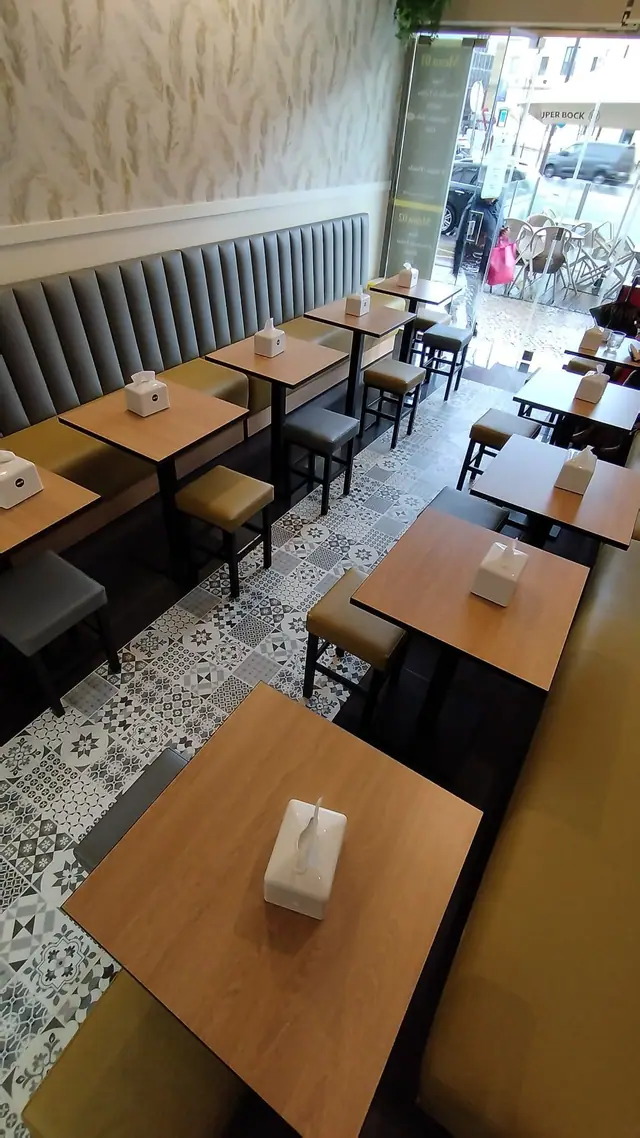 Sala vista de cima, com mesas alinhadas ao longo do banco corrido e a porta envidraçada para a rua