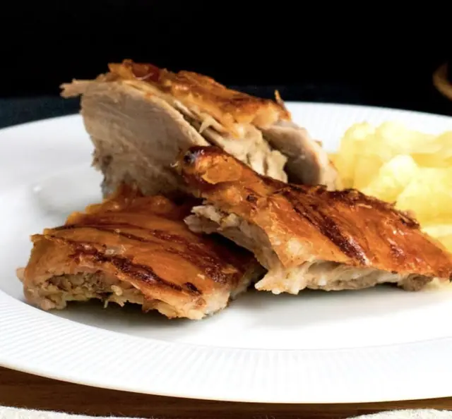 Pedaços de leitão assado num prato branco, com batatas fritas