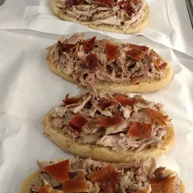 Sandes de leitão abertas, com a carne desfiada e pedaços de pele estaladiça